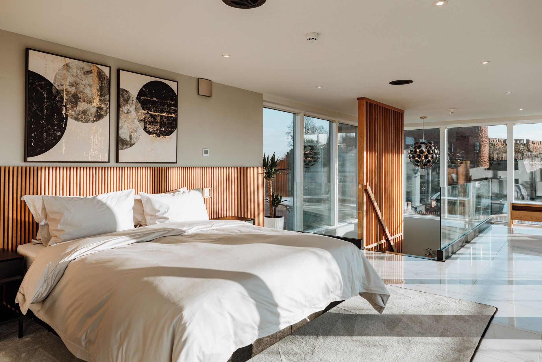 A modern bedroom with a large bed, a wooden headboard, and two abstract paintings on the wall.