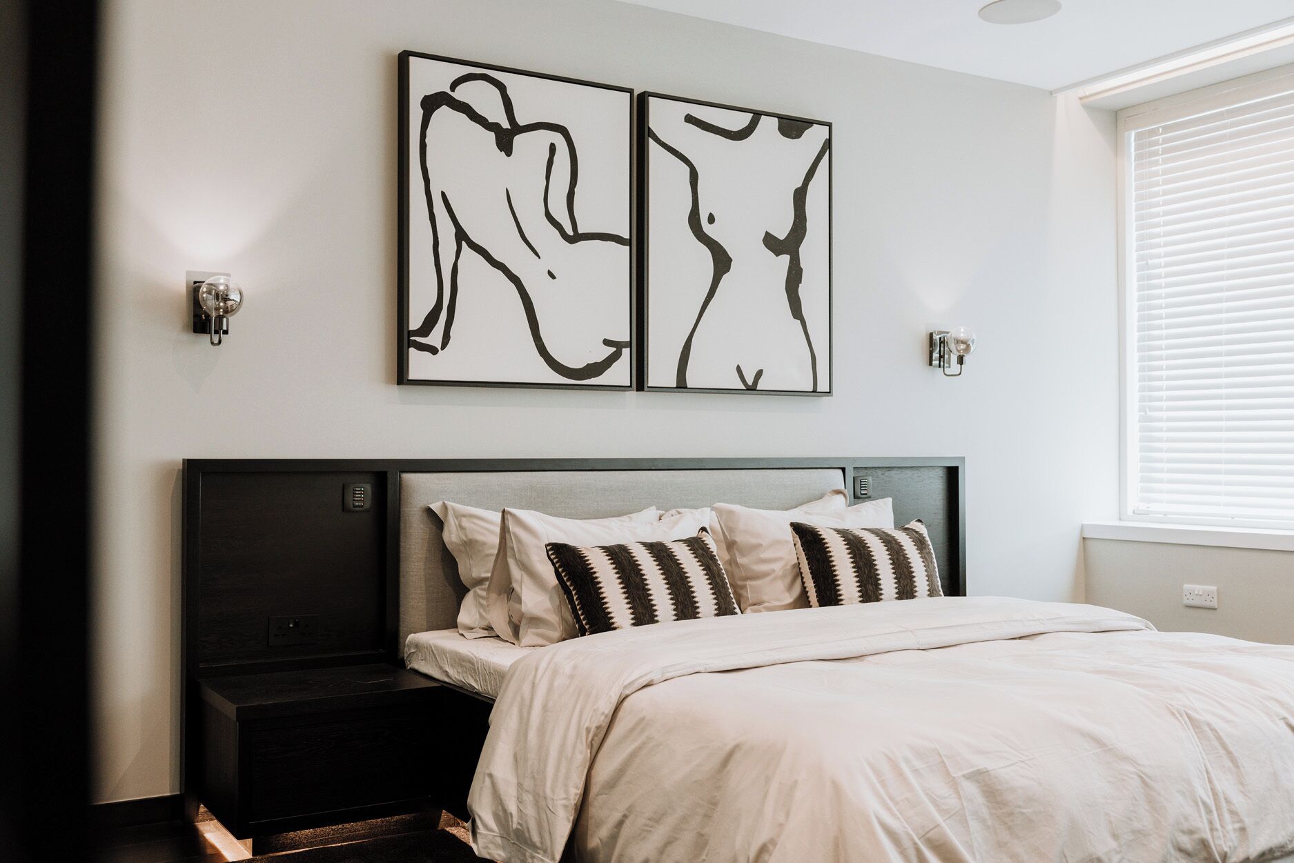 A bedroom with a bed, bedside tables, and abstract wall art.