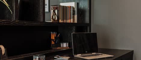 A desk with a laptop, a calculator, a notebook, and a cup of pens.