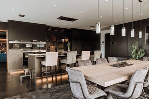 A modern kitchen with stainless steel appliances, a dining area with a wooden table and cushioned chairs, and pendant lighting. - Luxury two Story Penthouse With Roof top Terrace (Shrewsbury)