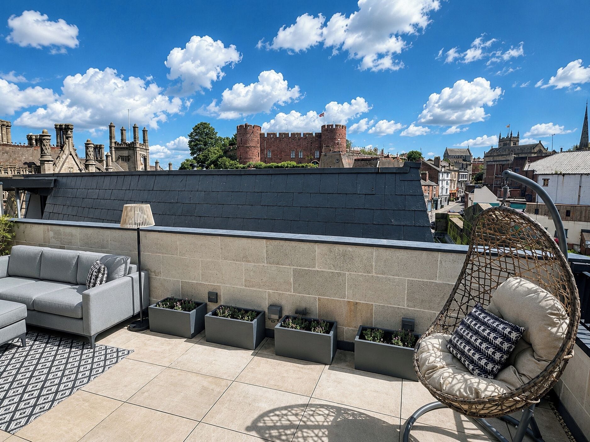 Une terrasse sur le toit avec un canapé gris, un fauteuil en osier et des jardinières.