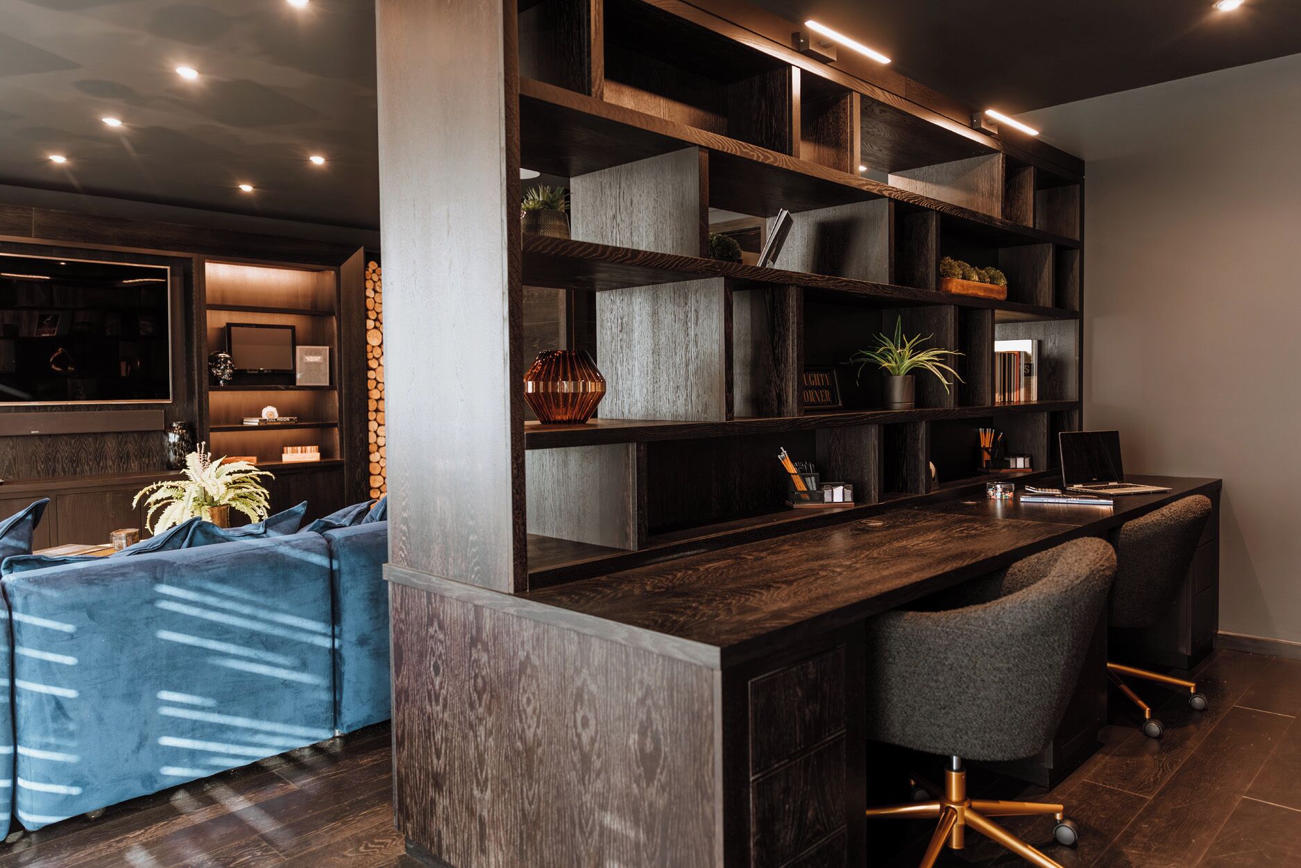 Een modern interieur met een donker houten bureau, een blauwe bank en een boekenkast.