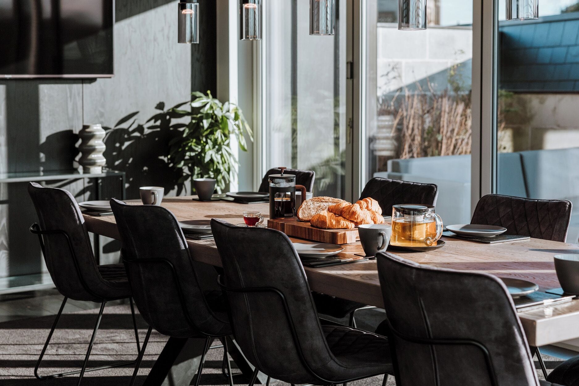 Una mesa de comedor con sillas, una cafetera, croissants y una taza de té.