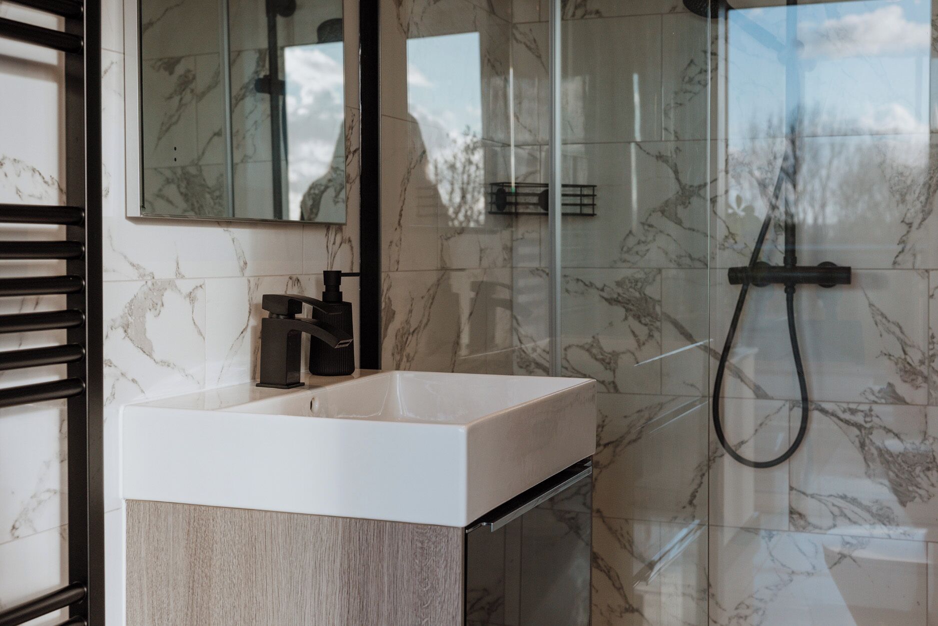 Un baño moderno con lavamanos blanco, grifo negro y cabina de ducha de vidrio.
