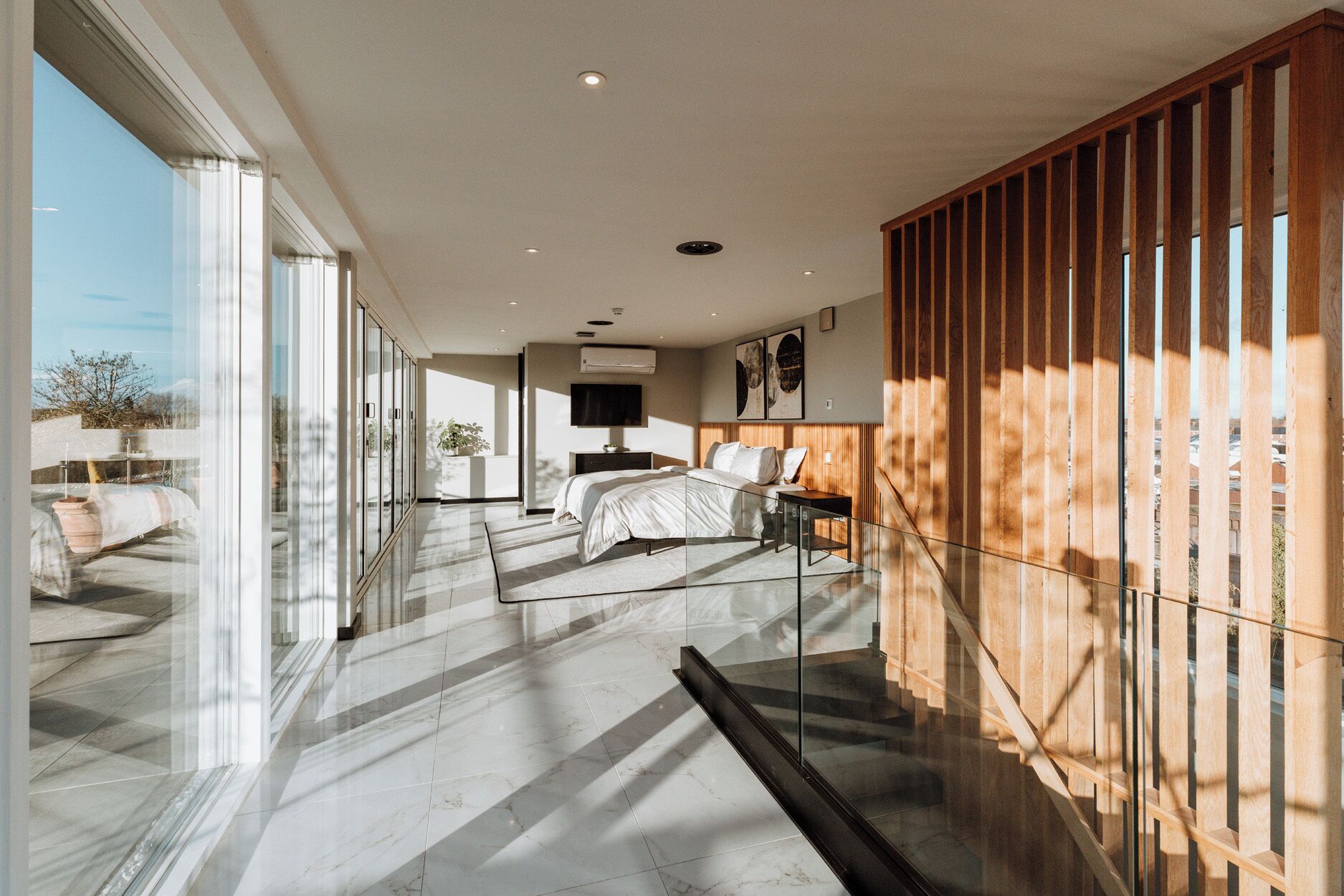 A modern bedroom with a large bed, a TV, and a balcony with a wooden railing.
