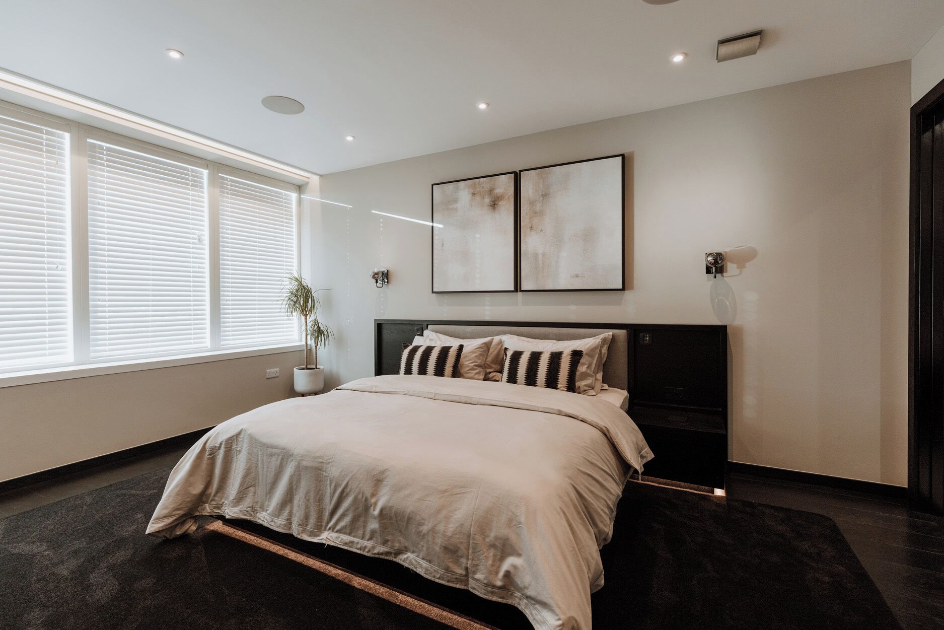 A modern bedroom with a large bed, a potted plant, and artwork on the wall.