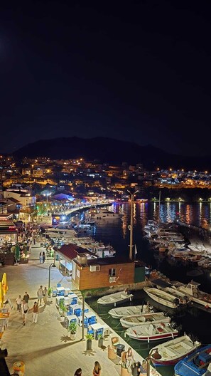 A nighttime view of a coastal town with a marina, boats, and a bustling waterfront area. - ADA MARİN SUİTE (Karaburun)
