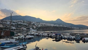 A marina with boats docked, a mountain in the background, and a town with buildings. - ADA MARİN SUİTE (Karaburun)