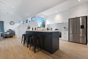 Eine moderne Küche mit Kochinsel, Barhocker, einem Edelstahl-Kühlschrank und einem Essbereich mit einer Couch und einem Couchtisch.