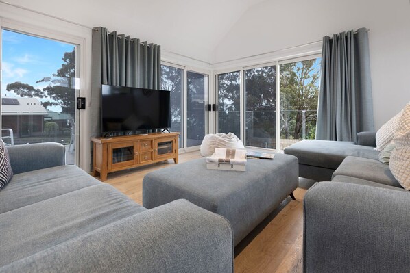 Ein modernes Wohnzimmer mit grauen Sofas, einem Holz-TV-Möbel und einem großen Flachbildfernseher.