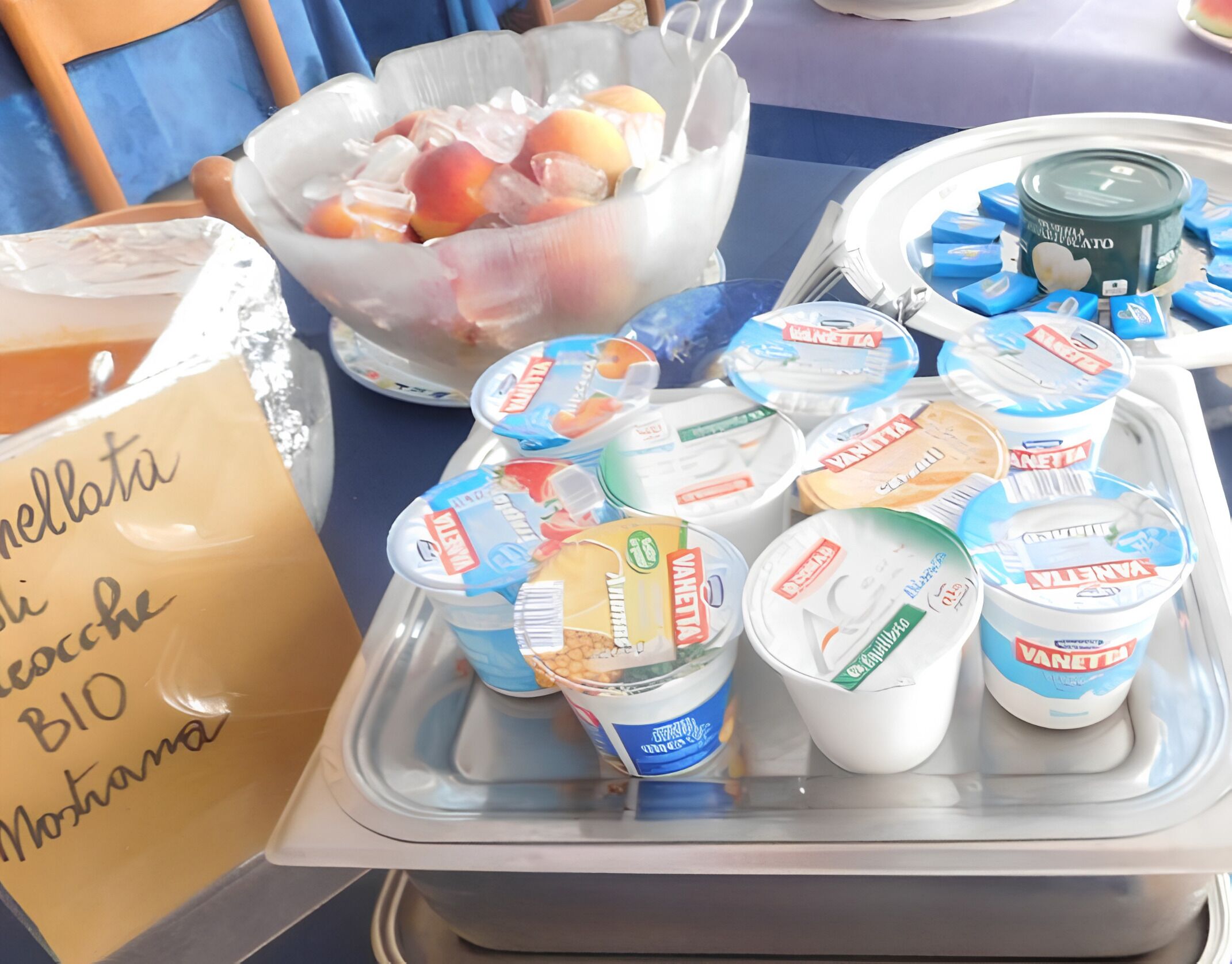 A table with yogurt containers, a bowl of fruit, and a container of butter.