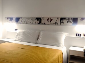 Una habitación de hotel con una cama, almohadas blancas, una colcha color mostaza, una obra de arte colgada en la pared y una mesita de noche con una lámpara.