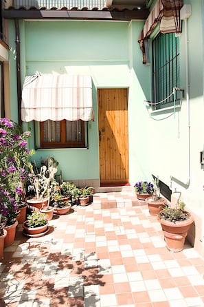 Une cour intérieure agrémentée de plantes en pot, une porte en bois et un sol carrelé.