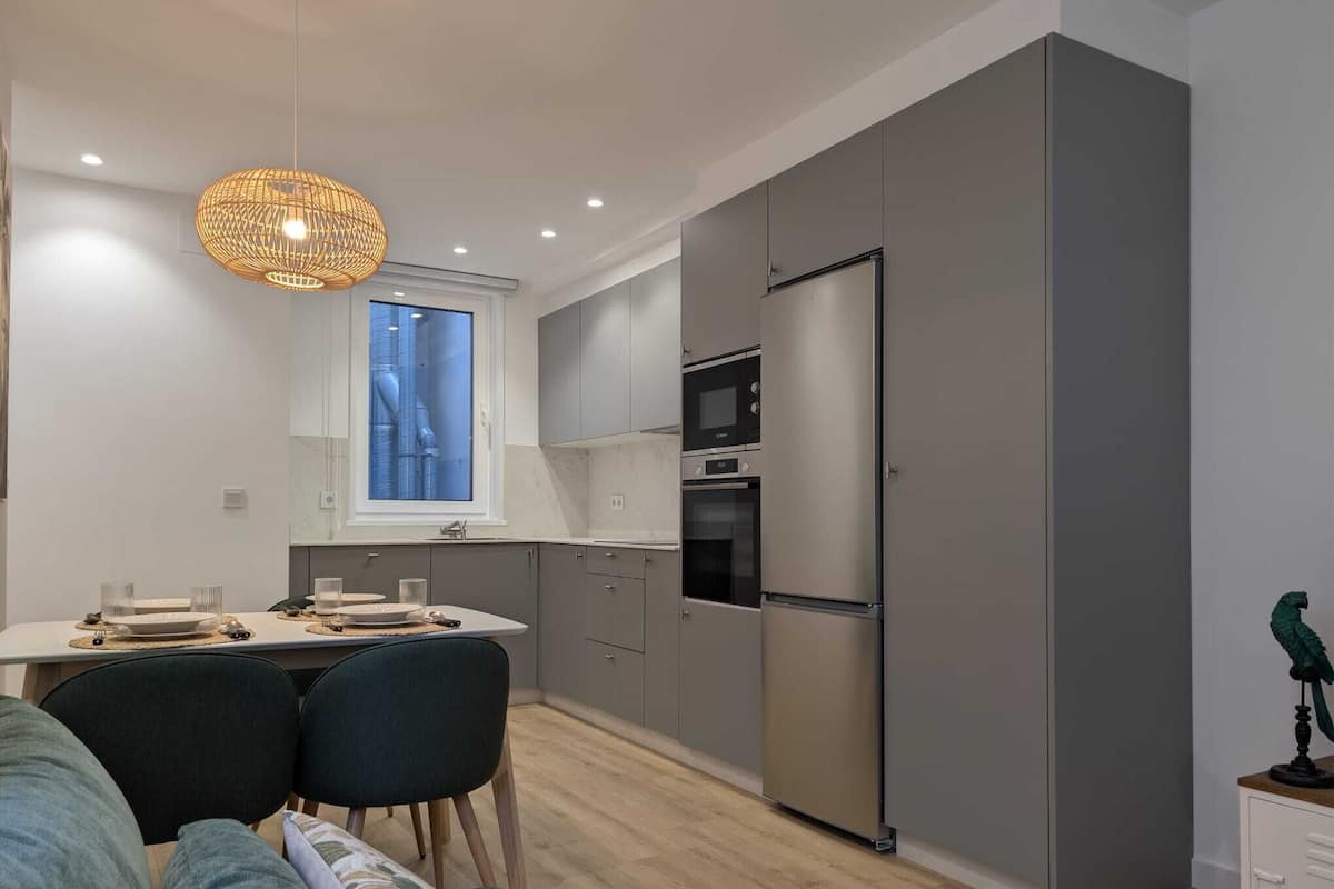 Une cuisine moderne avec des meubles gris, un réfrigérateur en acier inoxydable et un four encastré.