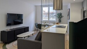 A modern living room with a flat-screen TV, a sofa, a dining table with chairs, a kitchen area, and a large window. - Paz Apartments By Como En Casa (A CORUÑA)