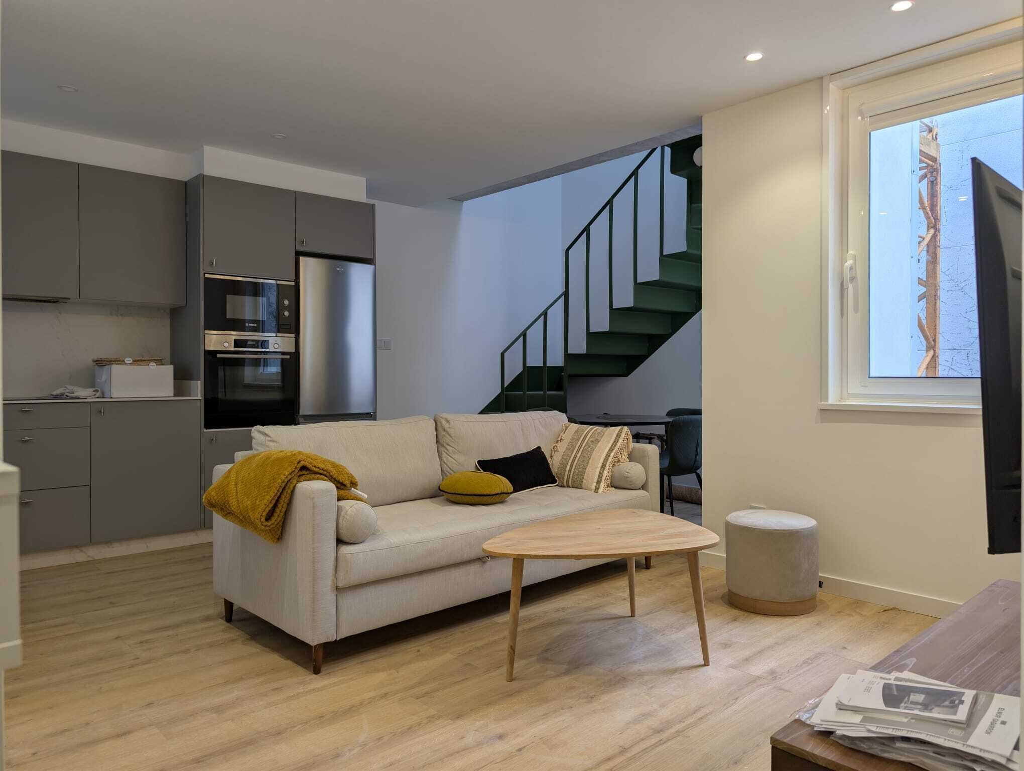 A modern living space with a sofa, coffee table, and kitchen area including a refrigerator and oven.