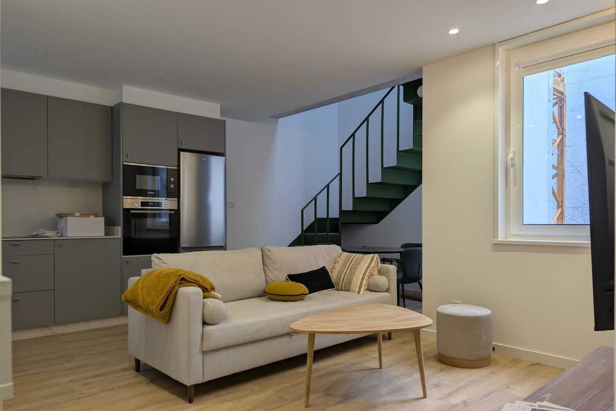 A modern living space with a sofa, coffee table, and kitchen area including a refrigerator and oven.