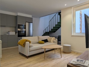 A modern living space with a sofa, coffee table, and kitchen area including a refrigerator and oven. - Paz Apartments By Como En Casa (A CORUÑA)