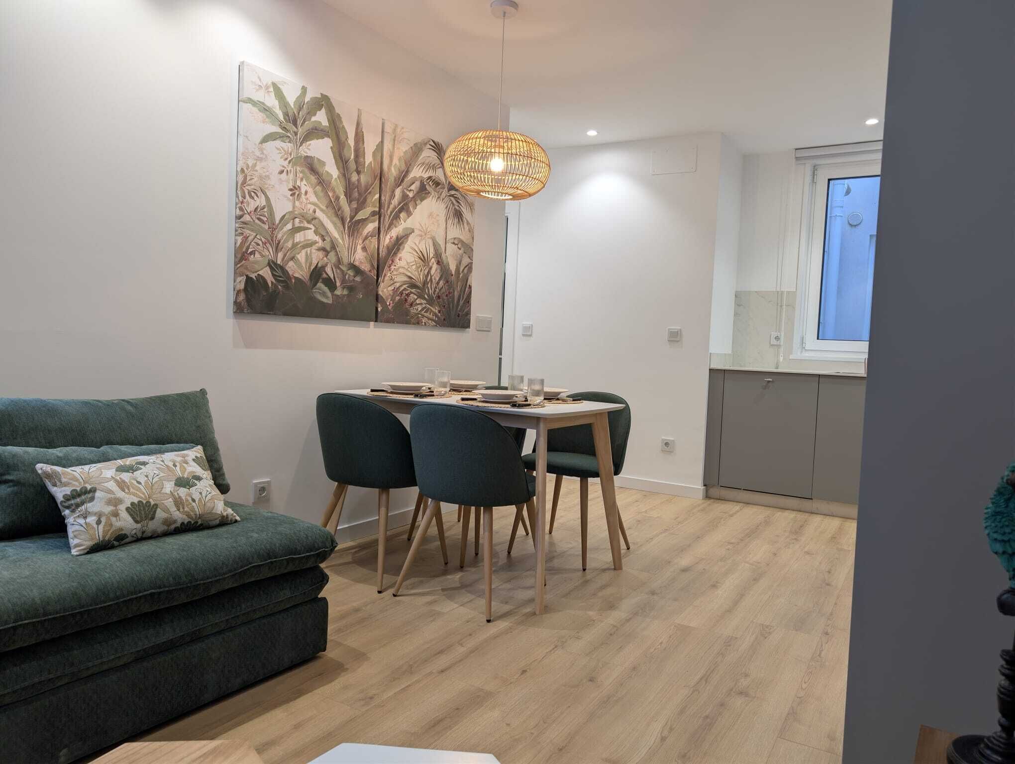 Una sala de estar moderna con un sofá, una mesa de comedor con sillas, una lámpara colgante y un mural grande en la pared.