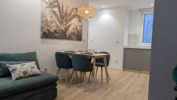 Una sala de estar moderna con un sofá, una mesa de comedor con sillas, una lámpara colgante y un mural grande en la pared.