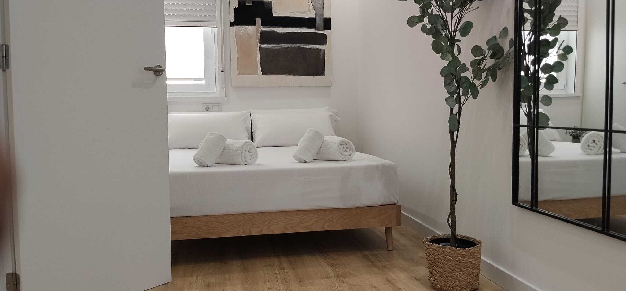 Un dormitorio con cama, toallas blancas, una planta en maceta y un espejo.