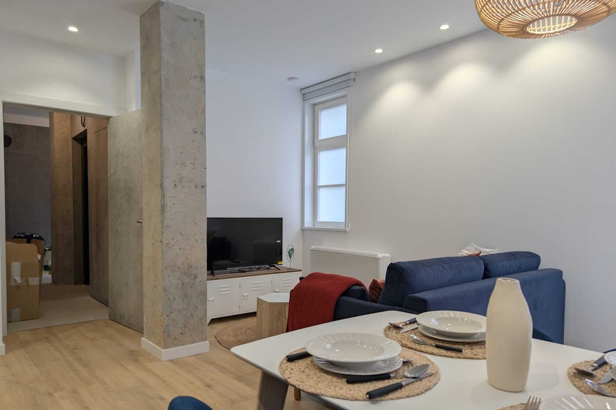 A modern living room with a TV, sofa, dining table, and a large window.