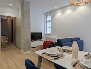 A modern living room with a TV, sofa, dining table, and a large window. - Paz Apartments By Como En Casa (A CORUÑA)