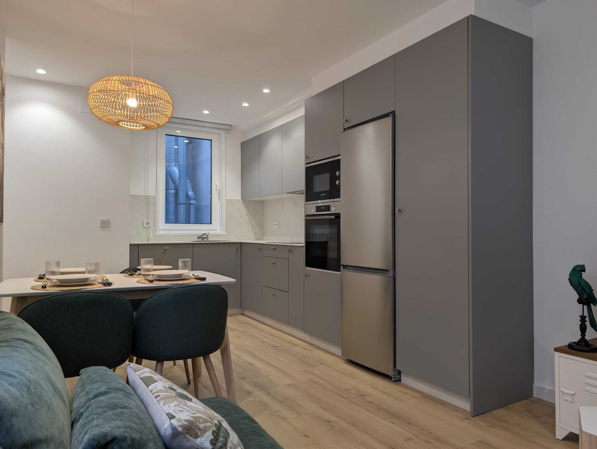 A modern kitchen with grey cabinets, a stainless steel refrigerator, and a built-in oven.