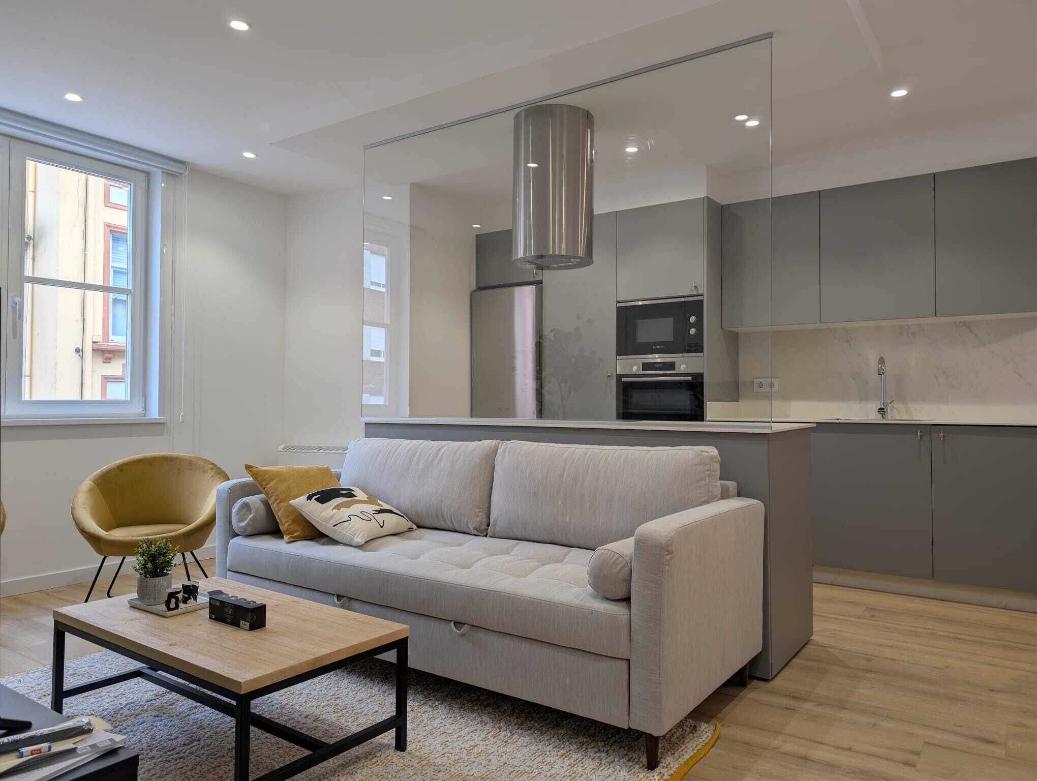 A modern living room with a sofa, a coffee table, and a kitchen area with a microwave and oven.