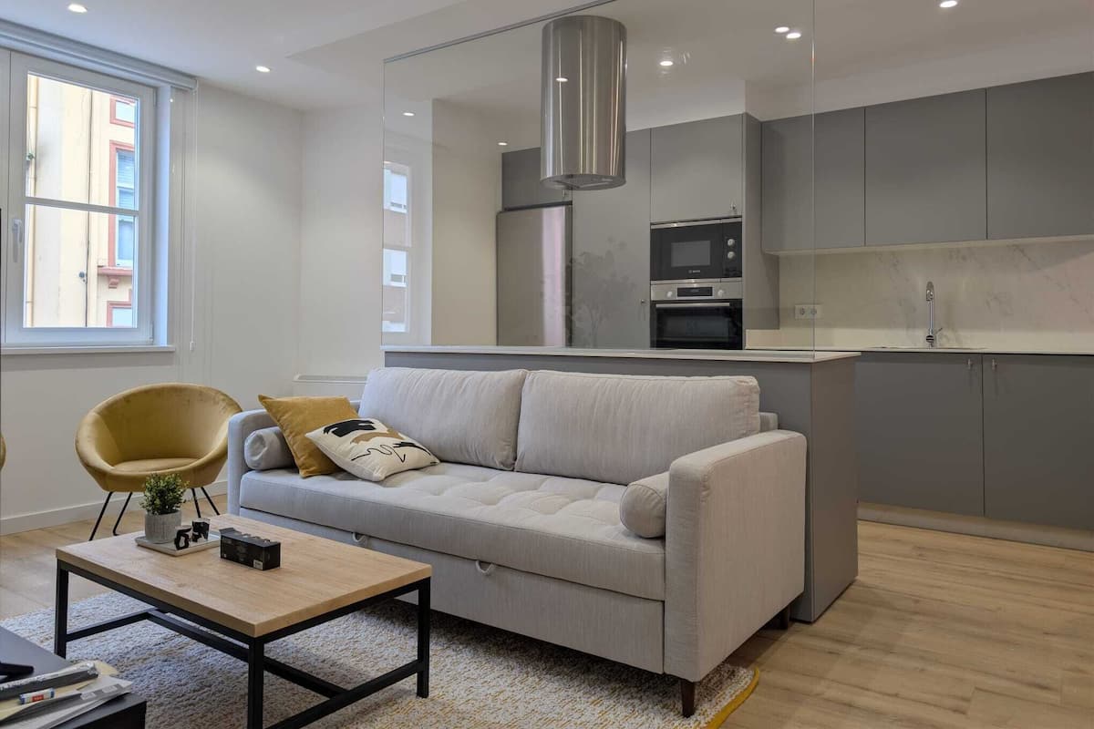 A modern living room with a sofa, a coffee table, and a kitchen area with a microwave and oven.