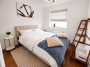 Ein Schlafzimmer mit Bett, Nachttisch, Fenster mit Jalousie, einer Strickleiter und einem Wandbild.