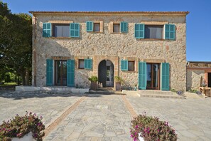 A stone building with multiple windows and doors, a paved courtyard, and potted plants.