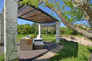 A covered outdoor seating area with a wooden deck, a wicker sofa, and a pergola.