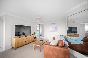 Ein stilvolles Wohnzimmer mit Flachbildfernseher, Holzmöbeln, einem Couchtisch und einem großen Spiegel.