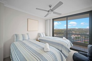 Een hotelkamer met twee bedden, een plafondventilator, een groot raam met uitzicht op het landschap, en een ingelijst schilderij aan de muur.