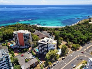 An aerial view of a coastal area with buildings, a road, and a beach. - Coastal Apartment with Ocean Views, Pool, Sauna & Tennis Court (Forster)