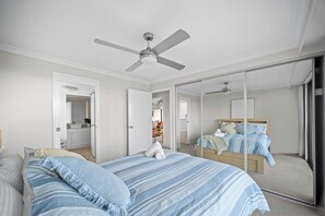 Ein Schlafzimmer mit Bett, Deckenventilator, großem Spiegel und einer Schiebetür zu einem anderen Raum.