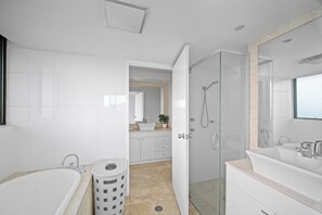 A modern bathroom with a bathtub, a glass-enclosed shower, a sink, and a mirror. - Coastal Apartment with Ocean Views, Pool, Sauna & Tennis Court (Forster)