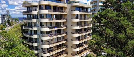 A multi-story residential building with balconies, surrounded by trees.