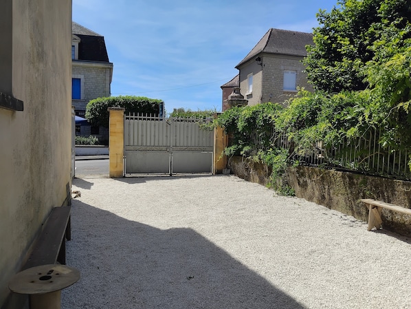 A gated driveway leading to a building with a stone facade, a bench, and a gravel path.