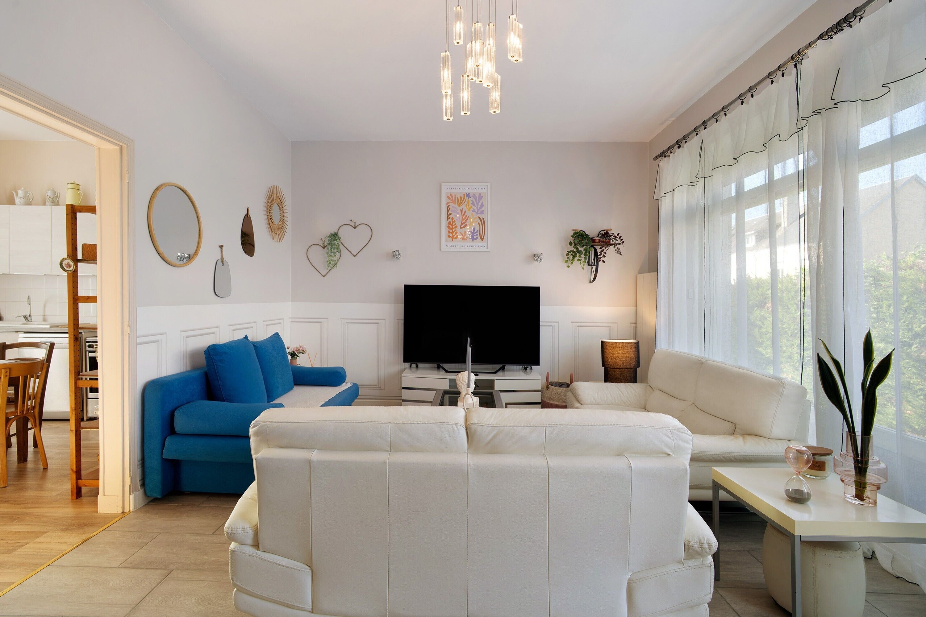 Ein Wohnzimmer mit einem weißen Sofa, einem blauen Sofa, einem Fernseher und einem Essbereich mit Holzsesseln.