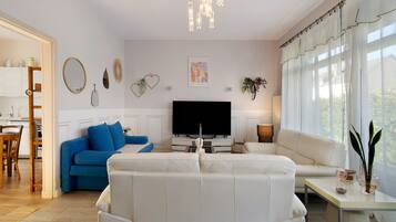 Ein Wohnzimmer mit einem weißen Sofa, einem blauen Sofa, einem Fernseher und einem Essbereich mit Holzsesseln.