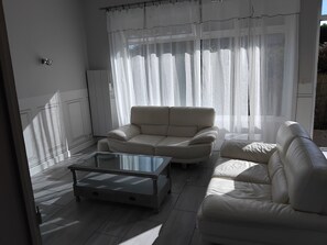 A living room with a beige sofa, a glass coffee table, and sheer curtains.