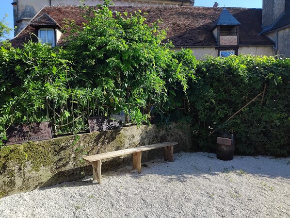 Un banc, une zone recouverte de gravier et un bĂątiment avec un toit en tuiles.