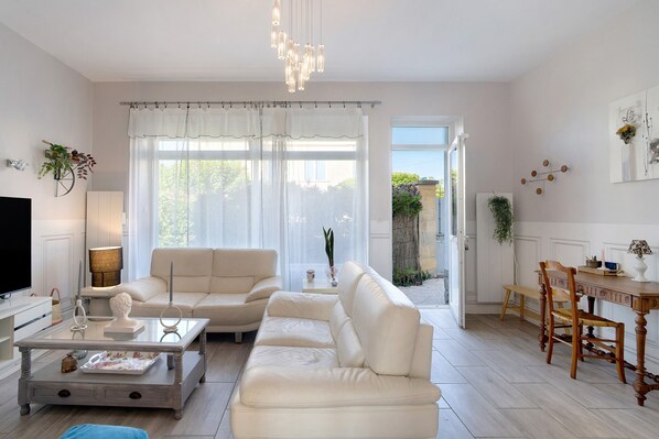 A living room with a sofa, coffee table, and TV. There is a dining area with a table and chairs.