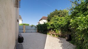 A gravel courtyard with a wooden bench, a large barrel, and a metal gate.