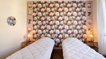 Ein Schlafzimmer mit zwei Betten, floralem Wandpapier, Nachttischlampen und einem runden Spiegel.
