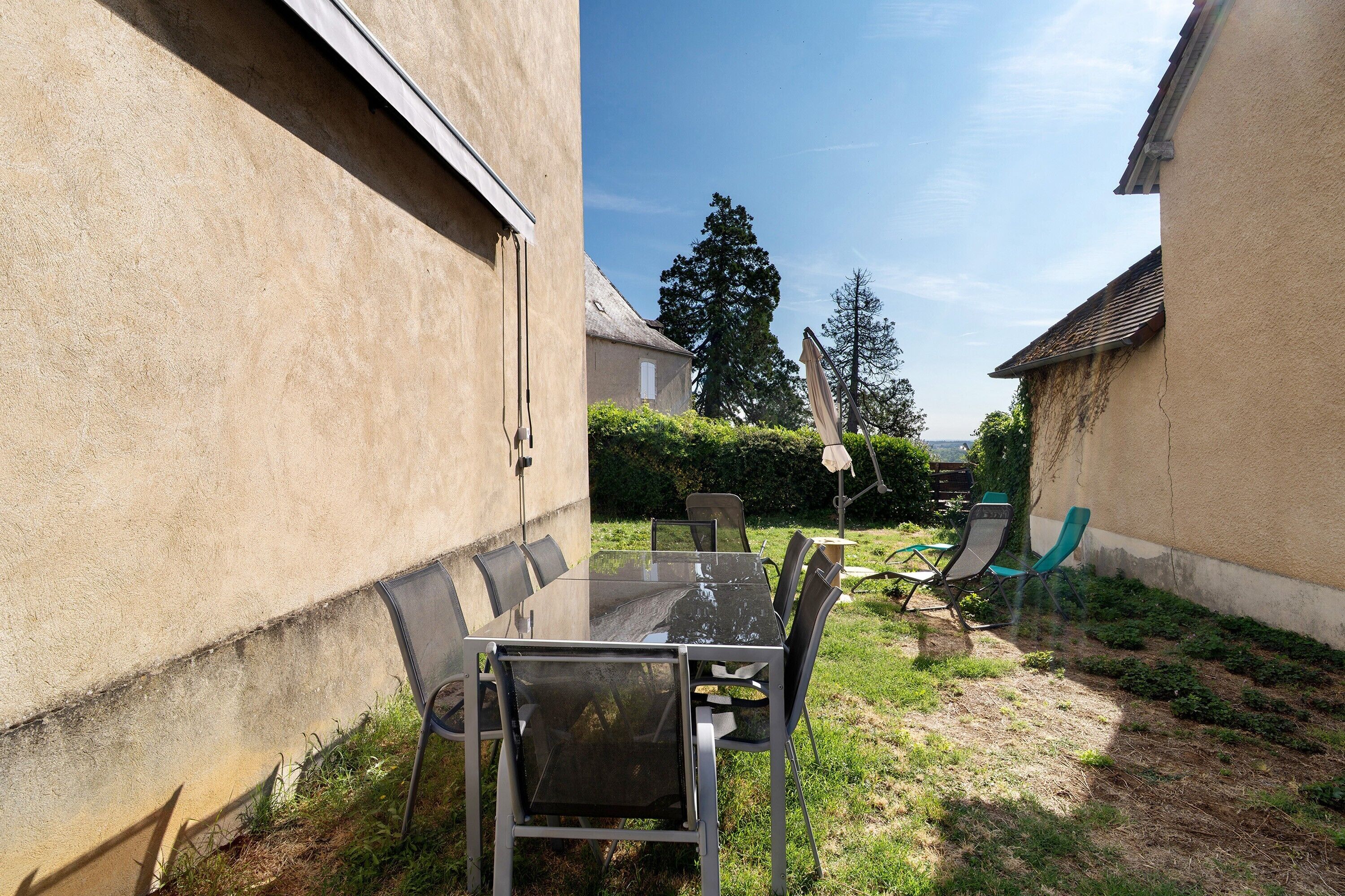 Un espace patio avec une table et des chaises en verre, entouré d’un petit muret et d’une pelouse.