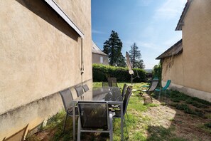A patio area with a glass table and chairs, surrounded by a low wall and a grassy area.