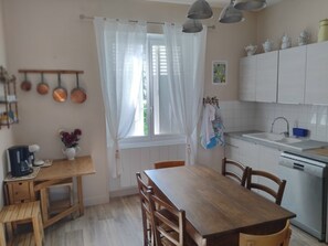 A kitchen with a dining table, chairs, a coffee maker, and a window with curtains.